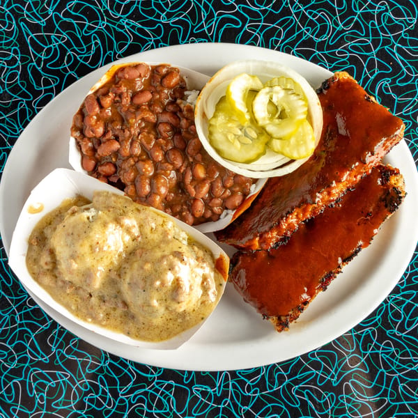 A Miss Delta BBQ plate with ribs, baked beans, gravy, and pickled onions and cucumbers.