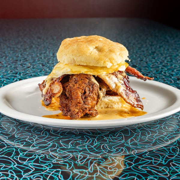 A Miss Delta fried chicken and bacon biscuit sandwich with gravy on a white plate.