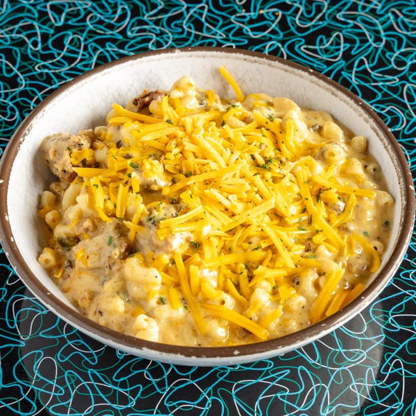 A bowl of Miss Delta's creamy mac and cheese, topped with shredded cheddar and herbs.
