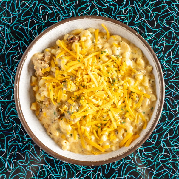 A bowl of Miss Delta's BBQ mac and cheese, topped with shredded cheddar and herbs.
