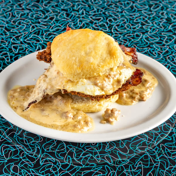 Miss Delta's biscuits and gravy with fried chicken and a fried egg on a white plate.