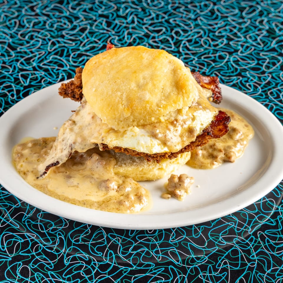 Miss Delta's biscuits and gravy with fried chicken and a fried egg on a white plate.