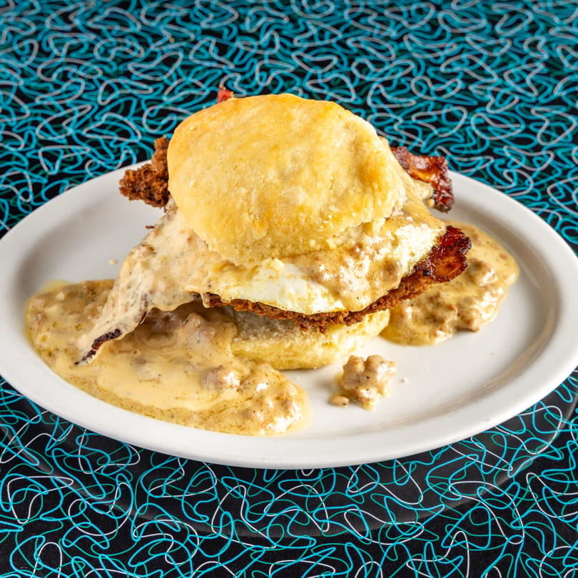 Miss Delta's biscuits and gravy with fried chicken and a fried egg on a white plate.