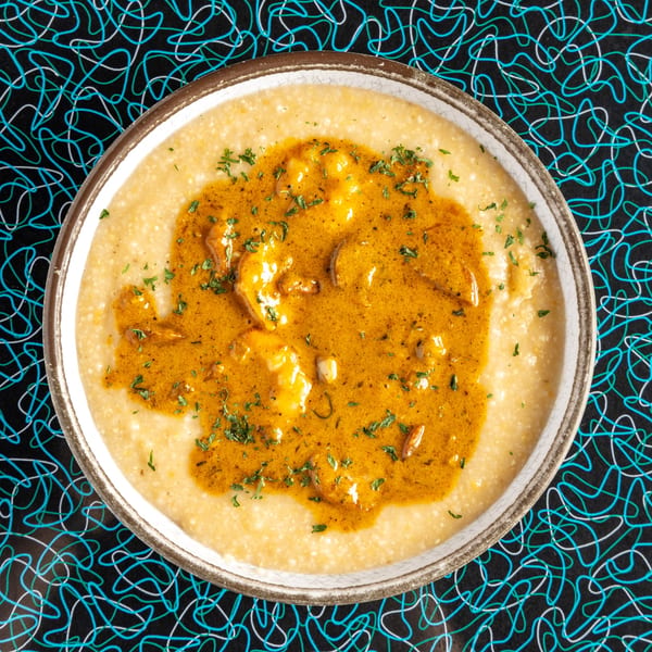 Miss Delta's shrimp and grits, a creamy dish with rich orange sauce and parsley, on a patterned table.